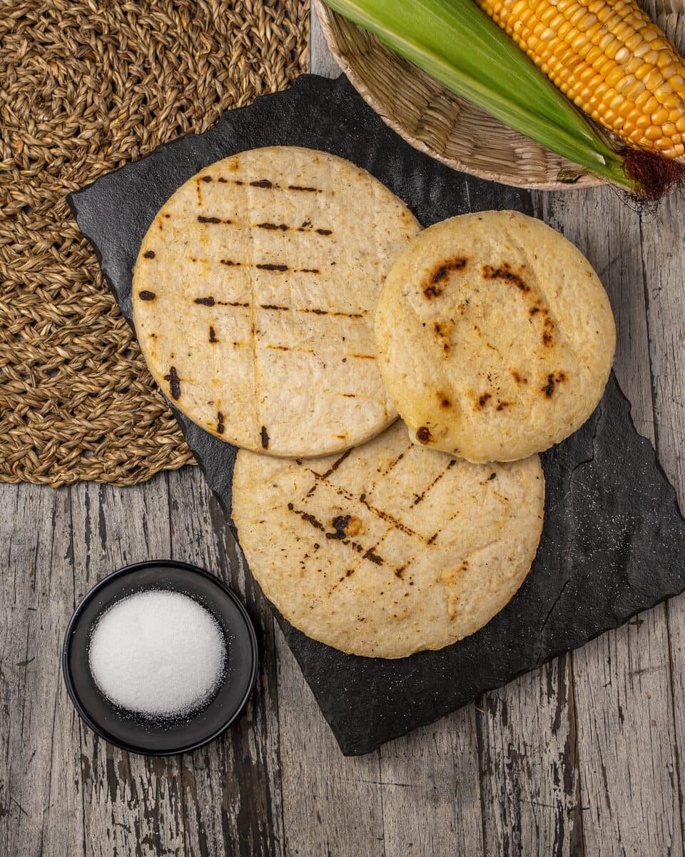 Arepas asadas sobre piedra junto a maíz y sal — los ingredientes de la receta tradicional